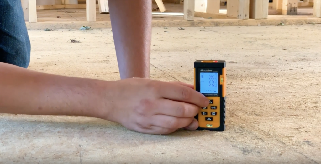 Hands Holding Laser Measurement Tool on the Ground