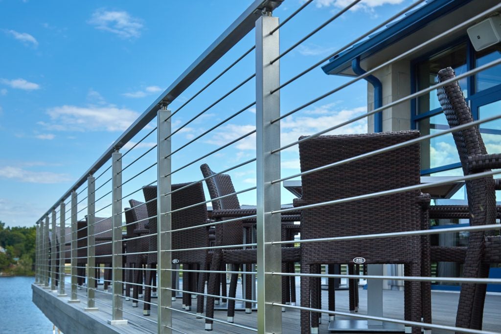 Stainless steel rod railing on an outdoor eating area with patio furniture overlooking the water