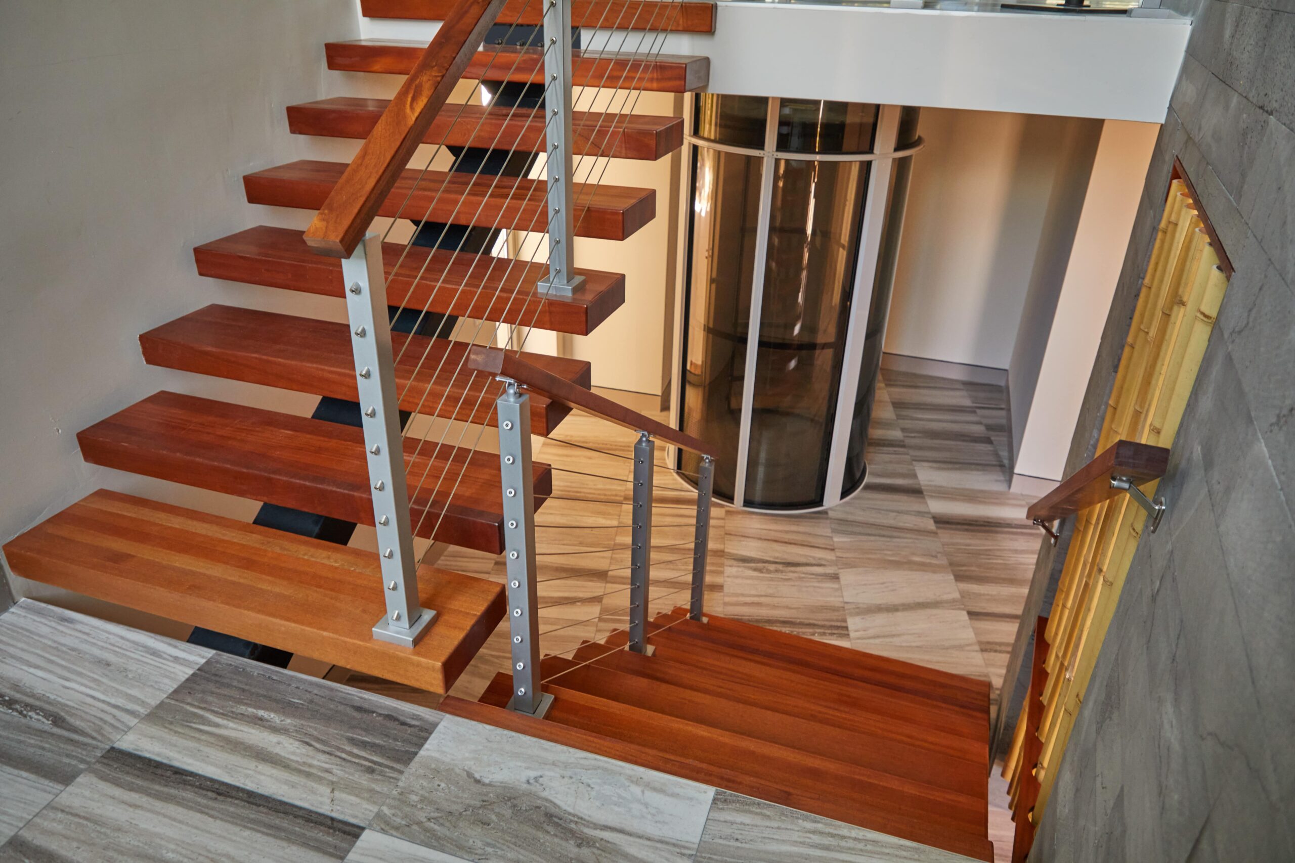 This stair design features floating steps with mahogany wood. There are small planks in a light-colored wood as the flooring.