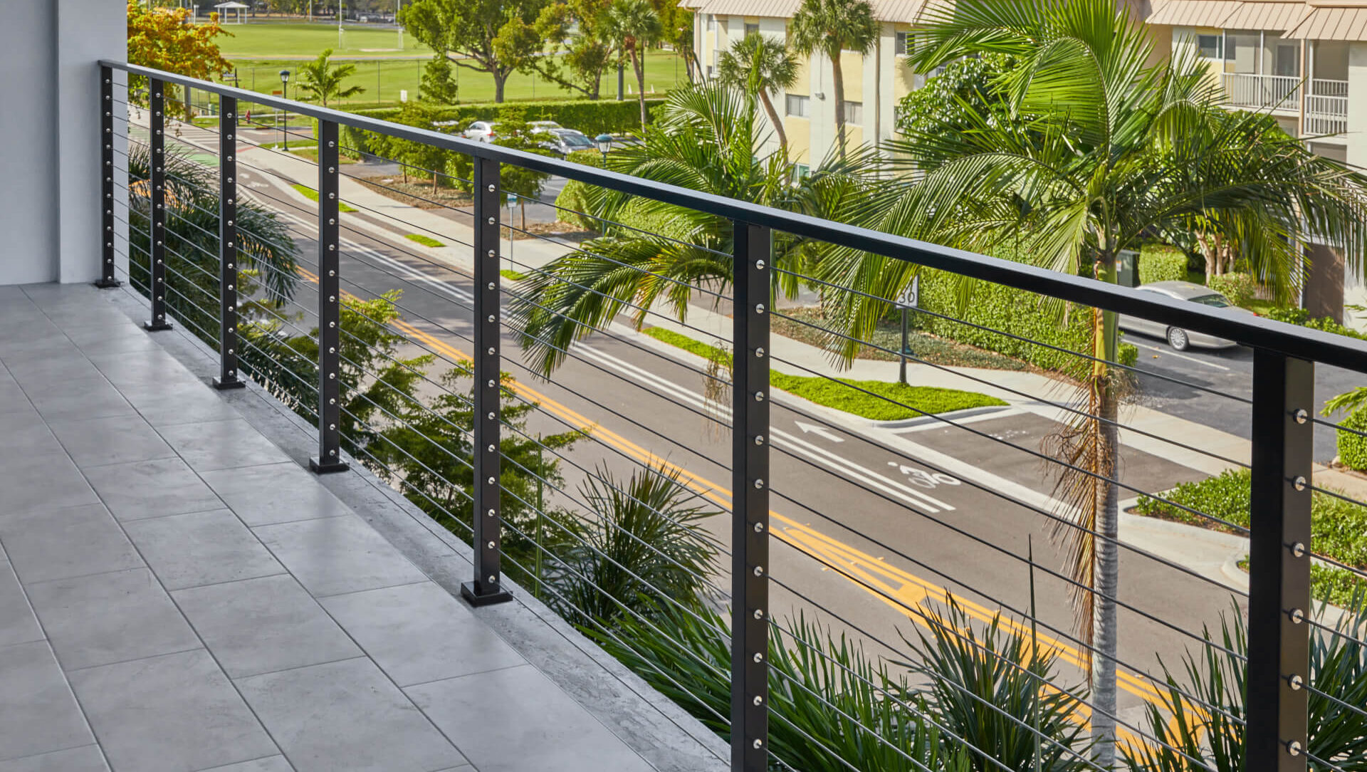 DIY cable railing on a deck overlooking a coastal street with palm trees in the background