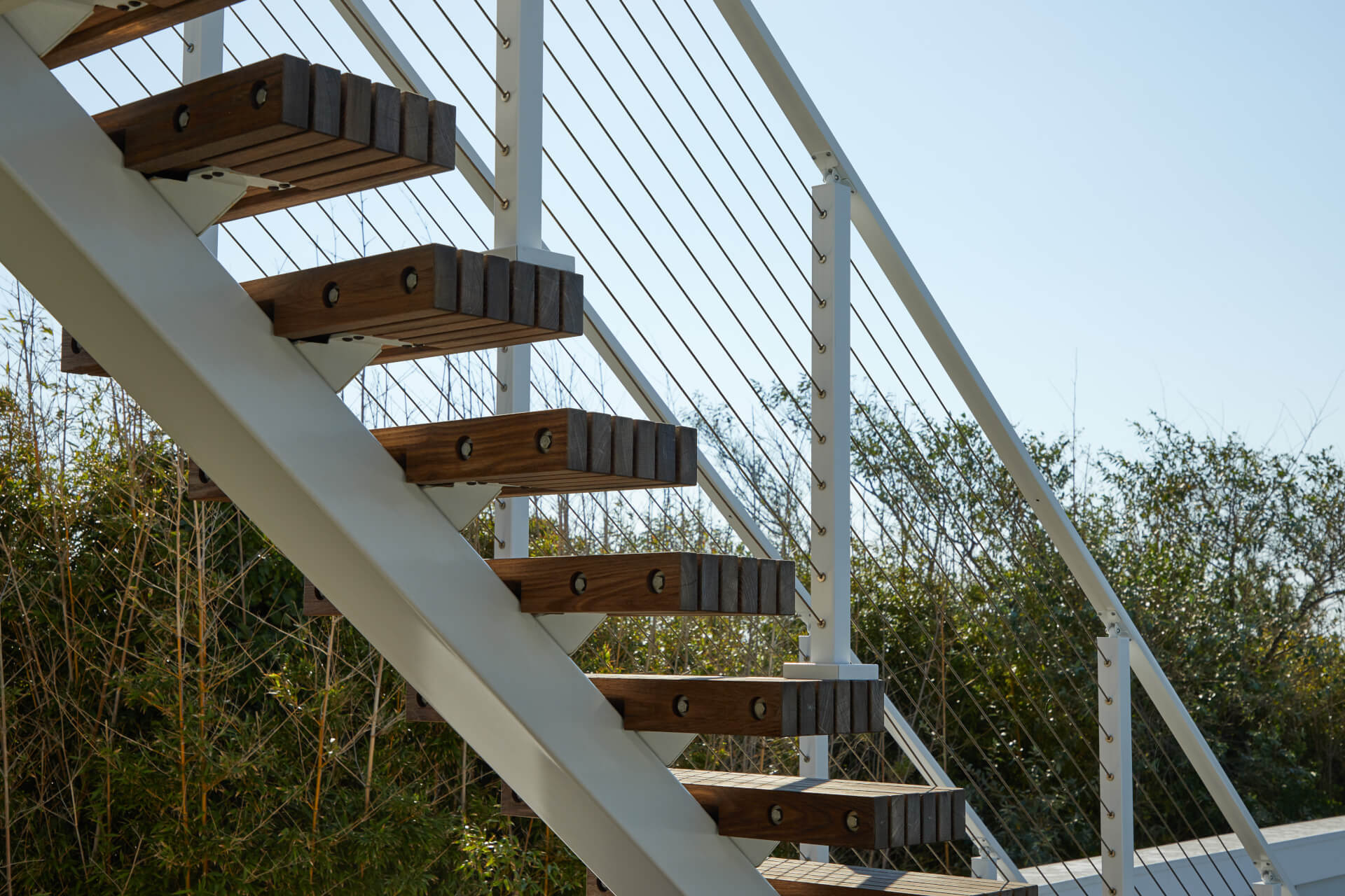 This staircase has dark wooden steps with floating treads and a metal handrail. There are green plants in the background.